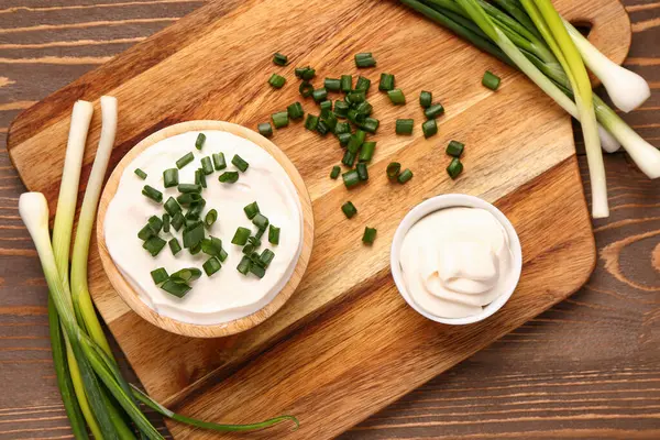 Ahşap arka planda dilimlenmiş yeşil soğanlı lezzetli ekşi krema kaseleri.