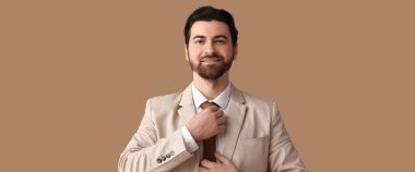 Şık takım elbiseli yakışıklı adam bej arka planda kravat ayarlıyor. 