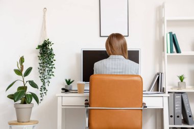 Ofisteki masada bilgisayarla çalışan genç bir kadın.