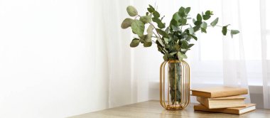 Pencerenin yanındaki masada okaliptüs dalları olan kitaplar ve vazolar. Tasarım için pankart