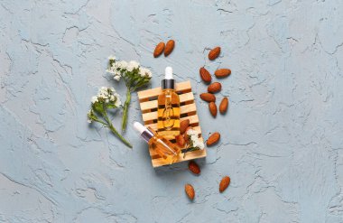 Güzel çiçekli kozmetik yağları ve mavi arka planda badem.