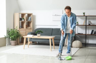 Genç adam süpürgeyle yerleri süpürüyor.