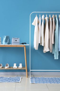 Mavi duvarın yanında şık kıyafetler, ayakkabılar ve aksesuarlarla dizilin.