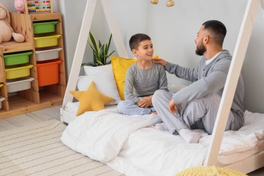 Pijamalı mutlu baba oğluyla evde yatakta konuşuyor.