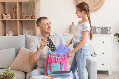 Babası küçük kızına okul çantasını toplaması için yardım ediyor.