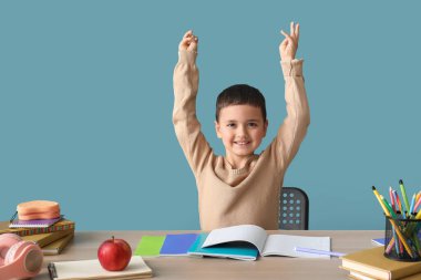 Küçük mutlu çocuk mavi duvarın yanındaki masada ödev yapıyor.