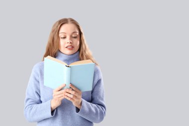 Gri arkaplan üzerine kitap okuyan kalın süveterli güzel bir kadın.