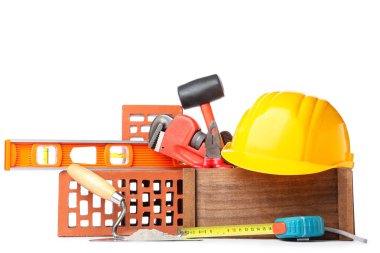 Kask, inşaat araçları ve beyaz arka planda tuğlalarla dolu bir kutu