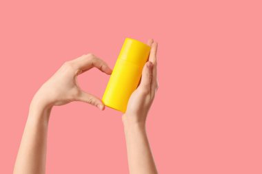 Kadın pembe arka planda güneş kremi şişesiyle kalp hareketi yapıyor.