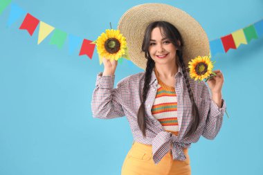 Hasır şapkalı, ayçiçekleri ve mavi arka planda bayrakları olan genç ve mutlu bir kadın. Junina festivali.