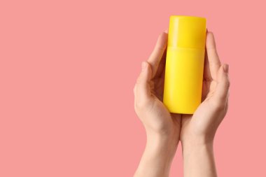 Pembe arka planda güneş kremi şişesi tutan kadın.