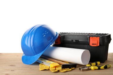 Beyaz arka plana karşı ahşap masadaki sert şapka, alet çantası ve inşaat araçları