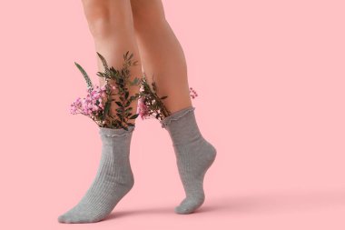 Pembe arka planda güzel çiçekleri olan gri çoraplı genç kadın bacakları.