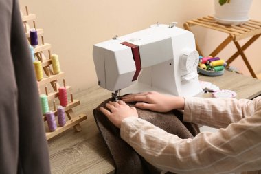 Dikiş makinesinde çalışan kadın terzi ve atölyede iplik makaralarıyla ayakta duruyor.