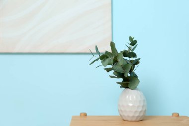 Mavi duvarın yanındaki masada okaliptüs dalları olan vazo, yakın plan.