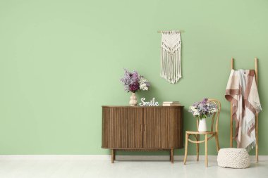 Sandalyeli, tuvaletli ve vazolarında leylak çiçekleri olan oturma odasının içinde.