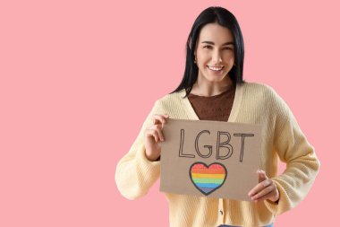 Pembe arka planda LGBT yazılı pankart tutan güzel genç bir kadın.