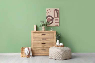 Çekmeceler, puf ve vazolar. Odanın içindeki yeşil duvarın yanında okaliptüs dalları var.