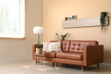 Oturma odasının içinde kahverengi kanepe, lamba ve masa var.