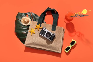 Kırmızı zemin üzerinde fotoğraf makinesi, tropikal yaprak ve plaj aksesuarları olan yaz kompozisyonu