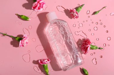 Bir şişe mikiler suyu, karanfil çiçekleri ve su damlaları pembe arka planda, yakın plan.