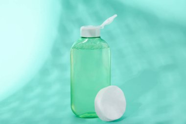 Turkuaz arka planda bir şişe mikiler suyu ve pamuk pedleri, yakın plan.