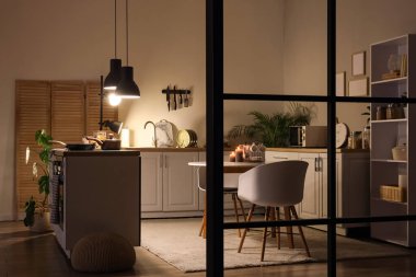 Beyaz tezgahlı mutfak, katlanan ekran ve geceleri parlayan lambalar.