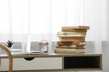 Işık odasındaki pencerenin yanındaki masaya yığınla kitap ve saat.