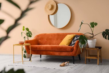 Rahat kahverengi kanepe, ev bitkileri ve odanın iç tarafındaki bej duvarın yanındaki masalar.