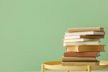 Yeşil duvarın yakınındaki sehpada yığınla kitap var.