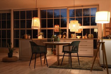 Akşamları tezgahları, yemek masası ve parlayan lambaları olan modern mutfak.