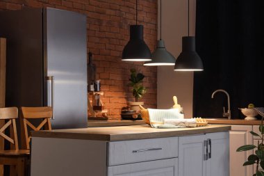 Tezgahta yumurtalı kap kacak ve karanlık mutfakta parlayan lambalar.