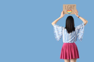 Mavi arka planda LGBT yazılı pankart tutan genç bir kadın.