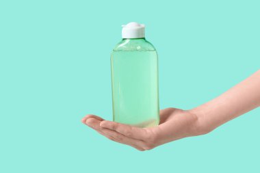 Yeşil arka planda bir şişe mikiler suyu olan kadın el, yakın plan.