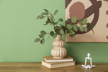 Okaliptüs dalları ve kitaplarla dolu vazo yeşil duvarın yanındaki odada, yakın plan.