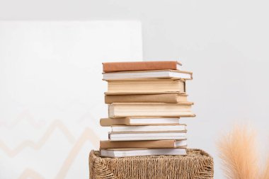 Hasır sepet ve beyaz duvarın yanındaki otlar üzerine yığınla kitap.