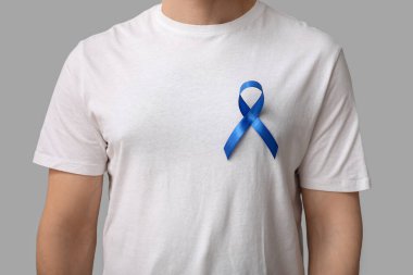 Tişörtünde gri arka planda mavi kurdele olan genç bir adam. Prostat kanseri farkındalığı