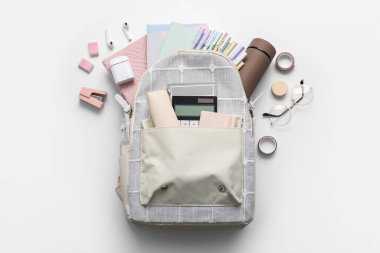 Farklı kırtasiye malzemeleri ve gri arka planda modern kulaklıklar olan şık bir okul çantası.