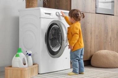 Evde çamaşır makinesini çalıştıran sevimli küçük kız. Çocuk tehlikede.