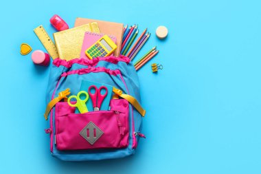Mavi arka planda farklı kırtasiye malzemeleriyle süslü okul çantası.
