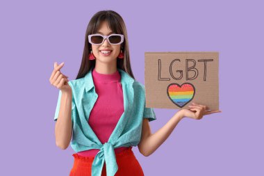 LGBT yazılı afiş tutan güzel bir genç kadın ve leylak arka planında kalp hareketi gösteriyor.