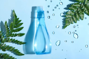 Bir şişe mikiler suyu ve mavi arka planda yeşil yapraklar, yakın plan.