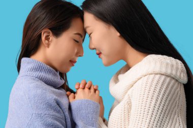 Güzel, mutlu Asyalı kız kardeşler mavi arka planda dua ediyorlar.