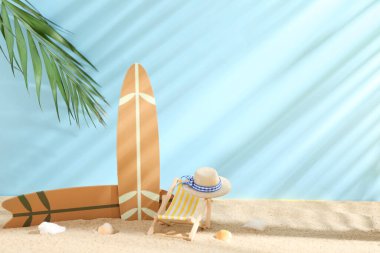Hasır şapkalı mini şezlong, sörf tahtaları ve kumdaki deniz kabukları mavi arka planda.