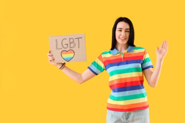 Sarı arka planda LGBT yazan bir pankart tutan güzel bir genç kadın.