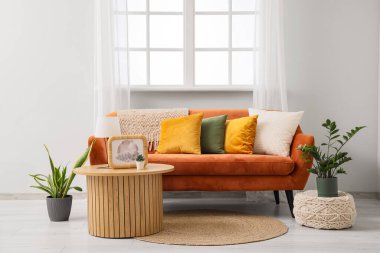 Rahat kahverengi kanepe, ev bitkileri ve oturma odasının iç tarafındaki pencerenin yanındaki puf.