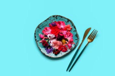 Farklı güzel, yenilebilir çiçekli tabaklar ve mavi arka planda çatal bıçaklar.