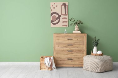 Çekmeceler, puf ve vazolar. Odanın içindeki yeşil duvarın yanında okaliptüs dalları var.