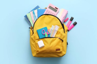 Sarı okul çantası ve mavi arka planda farklı kırtasiye malzemeleri.