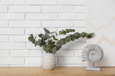 Okaliptüs dalları olan heykel ve vazo odadaki beyaz tuğla duvarın yanında, yakın plan.